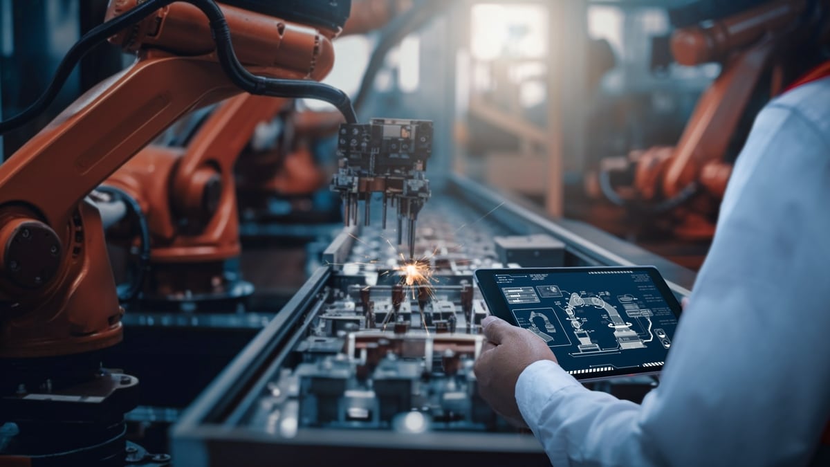 A production employee in manufacturing operates a robot arm with a digital tablet